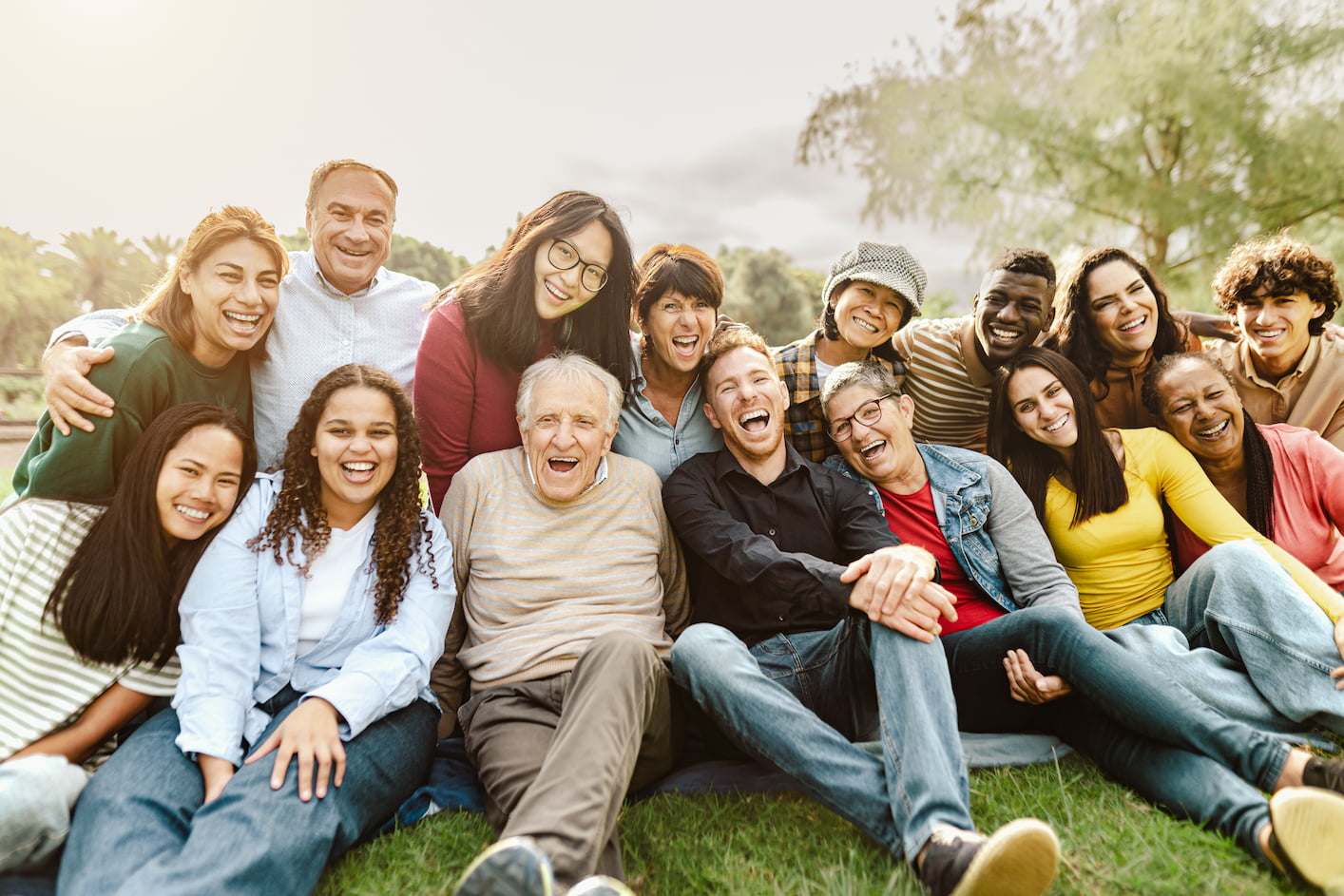 Happy multigenerational people having fun sitting on the grass in a public park